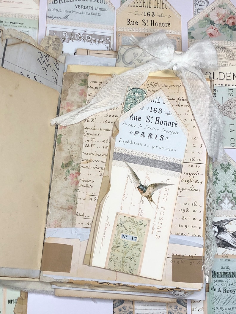 May include: A vintage postcard with a white lace bow and a bird illustration. The postcard has the text "163 Rue St. Honor&eacute; * PARIS * Exp&eacute;dition en province" and "CARTE POSTALE" printed on it. The postcard is decorated with a floral pattern and a small tag with the number "17" printed on it.