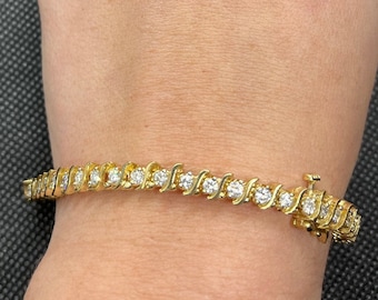 May include: A gold tennis bracelet with a row of round diamonds set in a wavy pattern.