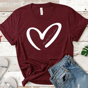 Op de afbeelding: Bordeauxkleurig T-shirt met een wit hart en de tekst "Math Teacher" in het hart.
