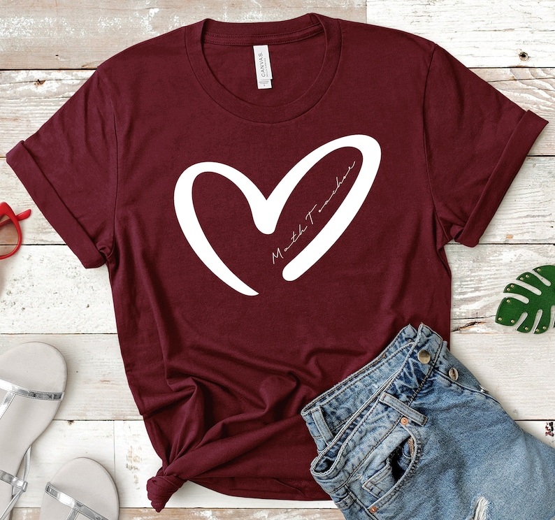 Op de afbeelding: Bordeauxkleurig T-shirt met een wit hart en de tekst "Math Teacher" in het hart.