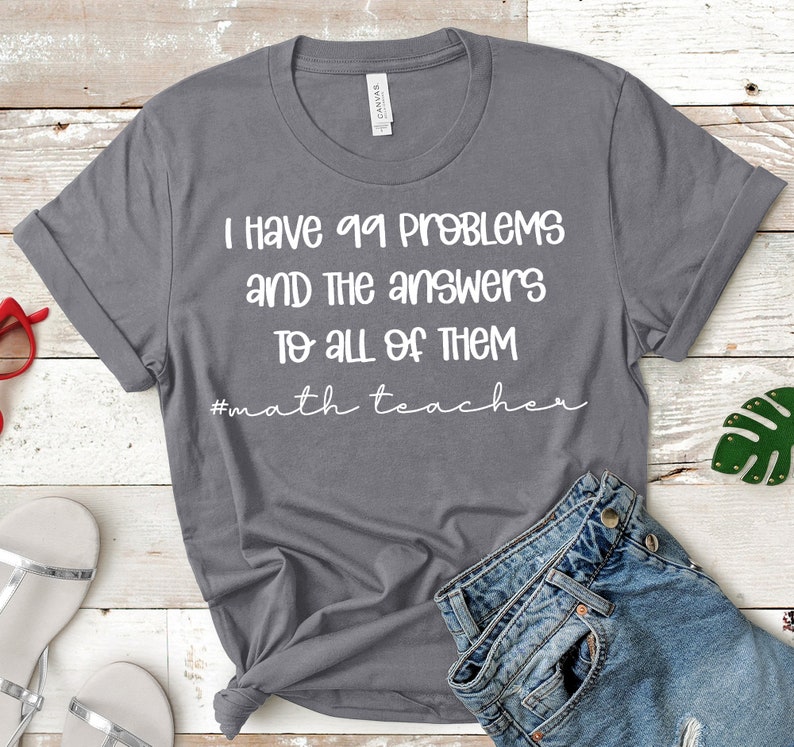Op de afbeelding: Grijs T-shirt met witte tekst die luidt "Ik heb 99 problemen en de antwoorden op alles #wiskundeleraar".