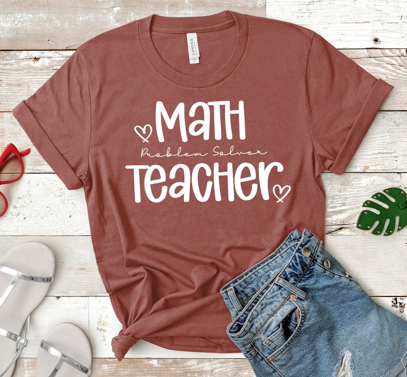 Op de afbeelding: Een maronkleurig T-shirt met witte tekst die "Math Problem Solver Teacher" luidt met een hartje aan weerszijden van de tekst.