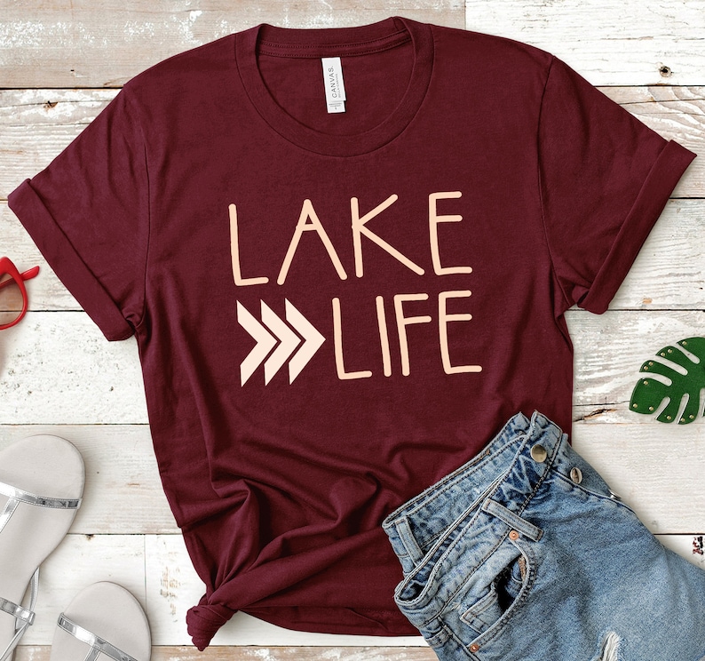 May include: A maroon t-shirt with the text "LAKE LIFE" in a peach color. The text is stylized with three arrows pointing to the right.