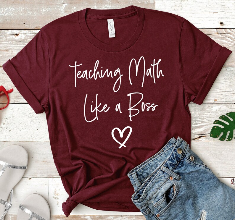 Op de afbeelding: Een maroon t-shirt met de tekst "Teaching Math Like a Boss" in witte letters en een wit hart.