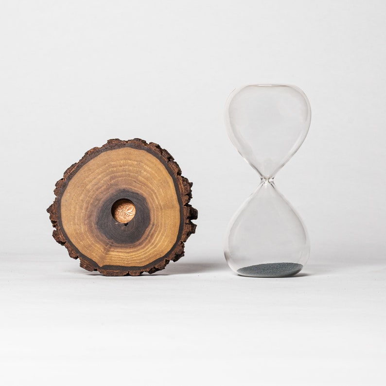 May include: A clear glass hourglass with black sand and a wooden tree ring base.