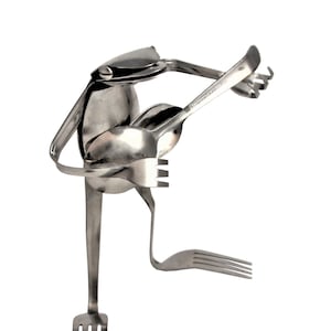 May include: A silver frog sculpture made from repurposed silverware. The frog is playing a guitar made from a spoon and fork.