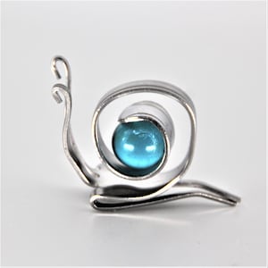 May include: A silver metal snail sculpture with a blue glass bead for a shell.
