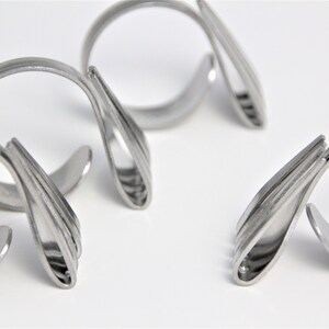 May include: Four silver napkin rings made from twisted silverware. The rings are designed to hold napkins in place at a formal dinner setting.