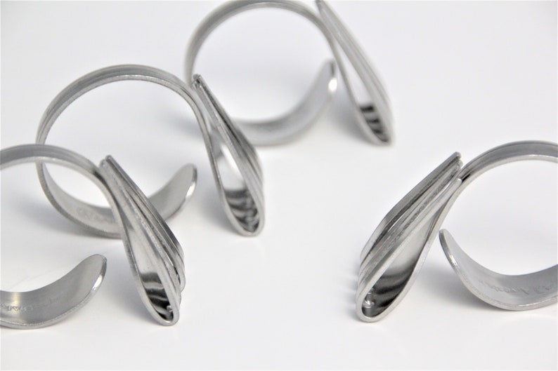 May include: Four silver napkin rings made from twisted silverware. The rings are designed to hold napkins in place at a formal dinner setting.