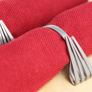 May include: Two silver napkin rings made of multiple thin metal strips, each ring is holding a red napkin.
