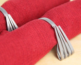 May include: Two silver napkin rings made of multiple thin metal strips, each ring is holding a red napkin.