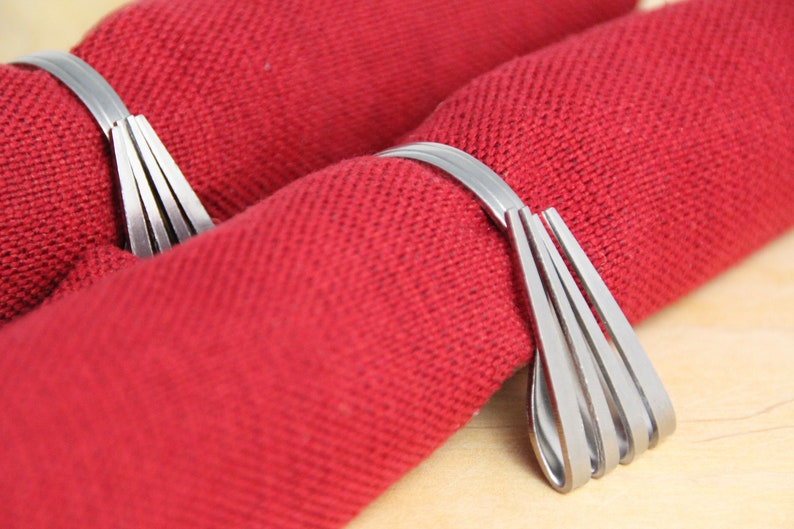 May include: Two silver napkin rings made of multiple thin metal strips, each ring is holding a red napkin.