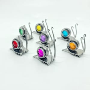 May include: A collection of whimsical metal snail figurines, each with a colorful, round glass shell. The shells are in various colors, including red, green, yellow, purple, blue, orange, and pink. The snails have a shiny, metallic finish.