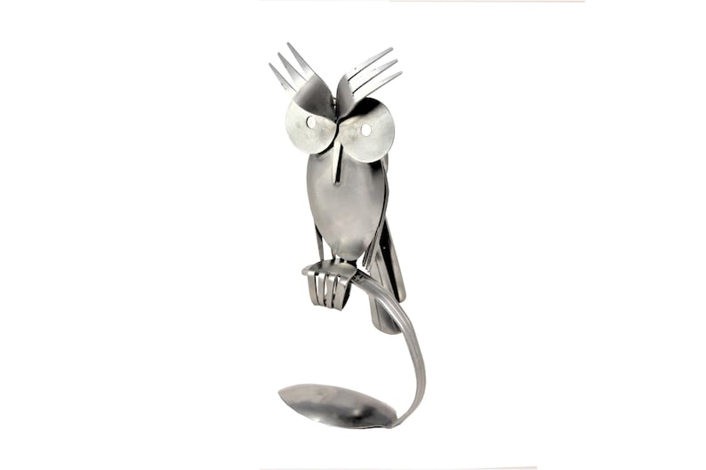 May include: A silver owl sculpture made from recycled silverware. The owl is perched on a branch made from a spoon.
