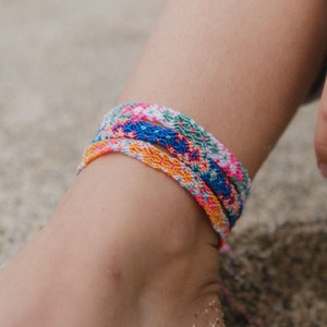 May include: Three colorful friendship bracelets with floral patterns in pink, blue, orange, and green colors.