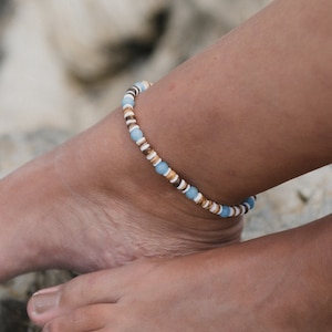 May include: A blue, white and brown beaded anklet. The anklet is made of small, round beads that are strung together on a thin cord.