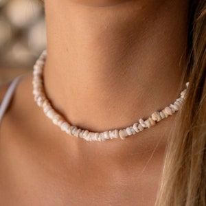 May include: A white shell choker necklace. The necklace is made of small, irregular shaped shells that are strung together on a thin cord.