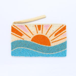 May include: A beaded clutch featuring a sunrise design. The clutch has a cream-colored background with an orange sun, pink and orange rays, and blue waves. It has a cream-colored wrist strap.