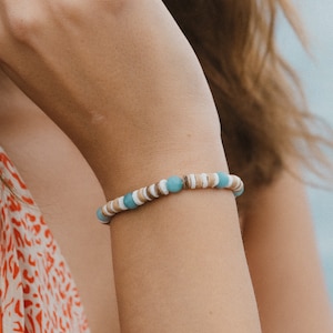 May include: A bracelet made of light brown and white wooden beads with turquoise blue accents.