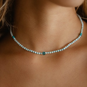 May include: A white and turquoise beaded necklace with a blue evil eye charm.