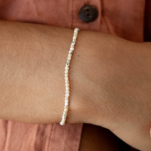 Peut inclure: Un bracelet en perles blanches et crème avec de petites perles rondes. Le bracelet est fait de matériaux naturels et a un design délicat et minimaliste.