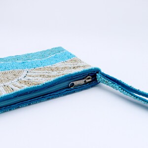 May include: A beaded clutch in shades of blue and cream, with a zipper closure and a matching beaded wrist strap. The clutch features a striped pattern with a fan-like design in the center.