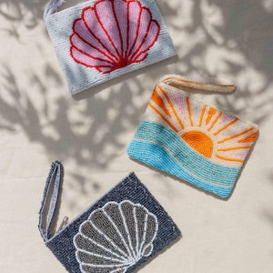 Puede incluir: Tres bolsos de mano con cuentas. Uno es azul claro con un diseño de concha rosa y roja. Otro presenta un amanecer sobre olas azules. El tercero es azul marino con un diseño de concha gris y blanca.