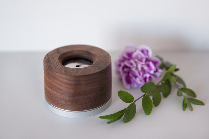 May include: A wooden and metal incense holder with a silver band around the bottom. The holder is sitting on a white surface next to a purple flower and green leaves.