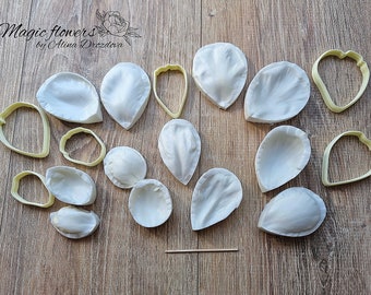 May include: A set of 14 silicone molds for making flower petals. The molds are white and come in various sizes and shapes. The molds are arranged on a wooden surface.