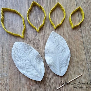 Könnte beinhalten: Vier gelbe, blattförmige Silikonformen und zwei weiße Silikonformen zum Herstellen von Polymer Clay Blättern. Die Formen befinden sich auf einer Holzoberfläche. Der Text "Magic Flowers by Alina Drozdova" ist in der unteren rechten Ecke des Bildes sichtbar.