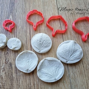 May include: A set of six white silicone molds for making hydrangea flower petals, and three red plastic cutters for shaping the petals. The molds are round and have a detailed design of hydrangea petals. The cutters are also round and have a scalloped edge.