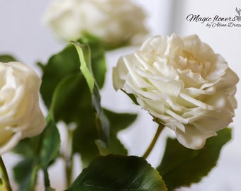 May include: Close-up of three white roses with green leaves. The roses are arranged in a bouquet and the image is focused on the center rose.