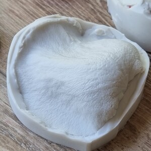 May include: A white silicone mold with a textured surface, resembling a furry animal paw print.
