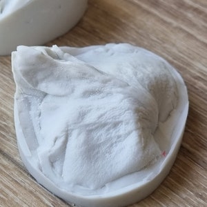 May include: A white silicone mold for making a small, detailed sculpture. The mold is shaped like a mountain or rock formation.