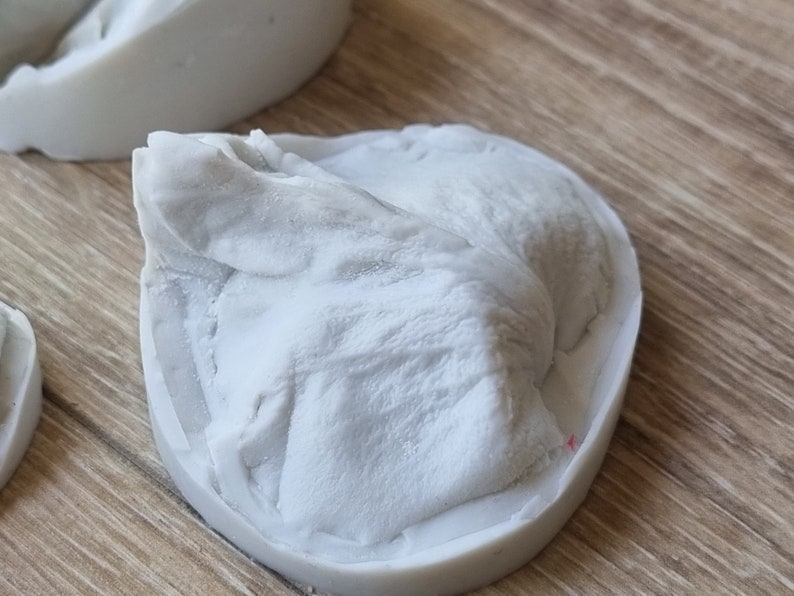 May include: A white silicone mold for making a small, detailed sculpture. The mold is shaped like a mountain or rock formation.
