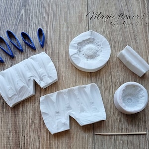 Puede incluir: Un conjunto de moldes de silicona blanca para hacer decoraciones florales. Los moldes tienen forma de hojas, pétalos y centro de flor. También hay varias herramientas de plástico azul para dar forma a las decoraciones.