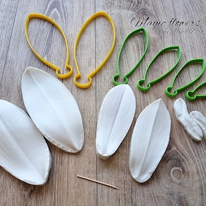 Puede incluir: Un conjunto de seis moldes de pétalos de flores de orquídea blancas y siete cortadores de plástico verde y amarillo para hacer flores de arcilla polimérica. El texto "Magic flowers by Alina Drozdlova" es visible en la imagen.