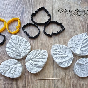 May include: A set of silicone moulds for making leaf-shaped decorations. The moulds are white and have a detailed leaf pattern. There are also black and yellow plastic cutters for creating leaves.