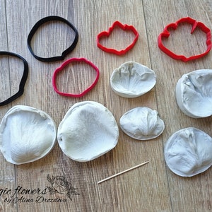 May include: A set of silicone molds and cutters for making polymer clay flowers. The set includes two large petal molds, three smaller petal molds, two round cutters, and two flower-shaped cutters. The molds are white and the cutters are red.