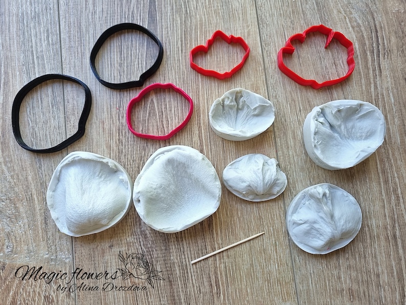 May include: A set of silicone molds and cutters for making polymer clay flowers. The set includes two large petal molds, three smaller petal molds, two round cutters, and two flower-shaped cutters. The molds are white and the cutters are red.