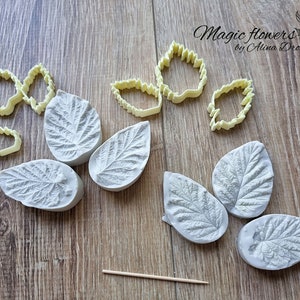 May include: A set of silicone moulds for making leaf-shaped decorations. The moulds are grey and have a detailed leaf pattern. There are also five yellow plastic leaf cutters.