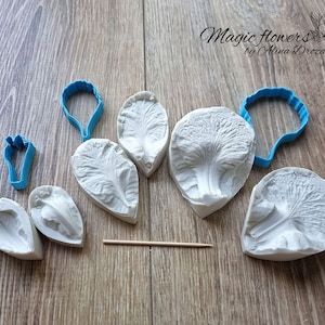 May include: A set of silicone moulds for making flower petals, featuring a variety of shapes and sizes. The moulds are white and are arranged on a wooden surface. The moulds are labelled "Magic Flowers by Alina Drozdlova".