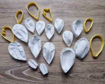 May include: A set of 15 white silicone molds for making flower petals. The molds are arranged on a wooden surface. The molds are different sizes and shapes, and some have a textured surface.