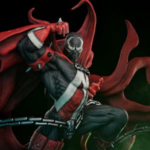 May include: A detailed figurine of the comic book character Spawn, in a dynamic pose. The figure is predominantly black and gray, with red accents on the cape, gauntlets, and boots. The figure has a white emblem on the chest and a silver chain.