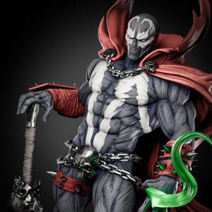 May include: A highly detailed Spawn action figure featuring a muscular dark grey body with white chest markings, a flowing red cape, and a silver chain belt with a skull buckle. The figure wears spiked red wristbands and holds a spiked mace weapon.