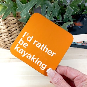 Op de afbeelding: Oranje vierkante onderzetter met de tekst "I'd rather be kayaking" in wit.