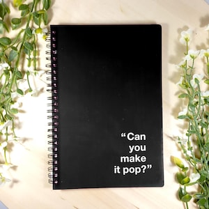 以下が含まれることがあります： 表紙に白い文字で「Can you make it pop?」と書かれた黒いスパイラルノート