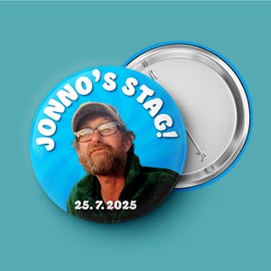May include: A circular pin-back button featuring a photograph of a bearded person wearing glasses and a cap. The blue background includes the white text JONNO'S STAG! and the date 25. 7. 2025. The back of the button shows a metal pin mechanism.