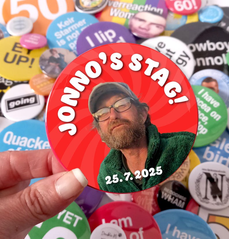 May include: A circular pin-back button featuring a red background with a swirling pattern. The button displays a photograph of a person with a beard wearing a cap and glasses, the text JONNO'S STAG! in white, and the date 25.7.2025 in white.
