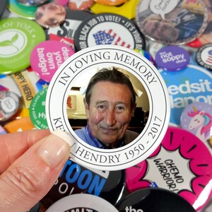 May include: A white button with black text that reads "In Loving Memory Kevin Hendry 1950 - 2017". A photo of a man is in the centre of the button.